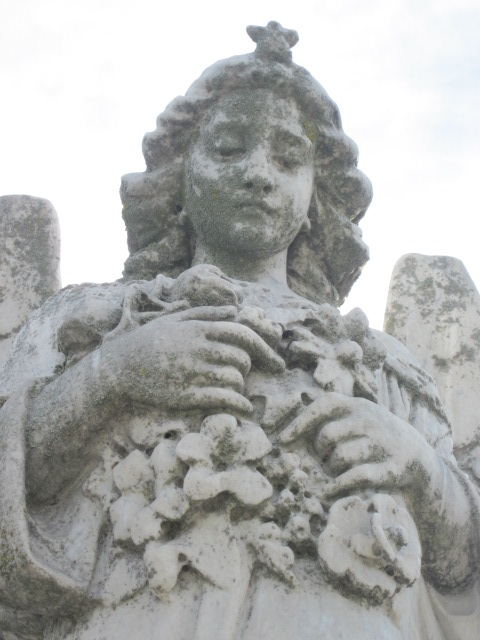 cement angel outside in cemetary, holding lilies