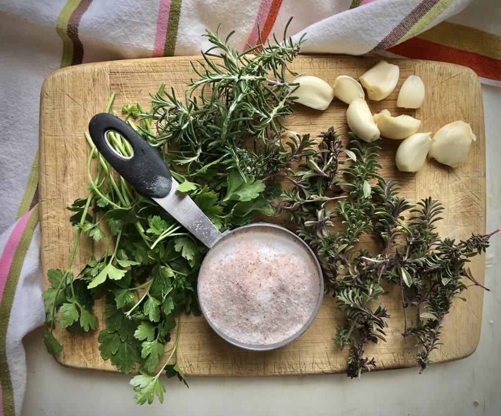 board with garlic cloves, fresh herbs and kosher salt