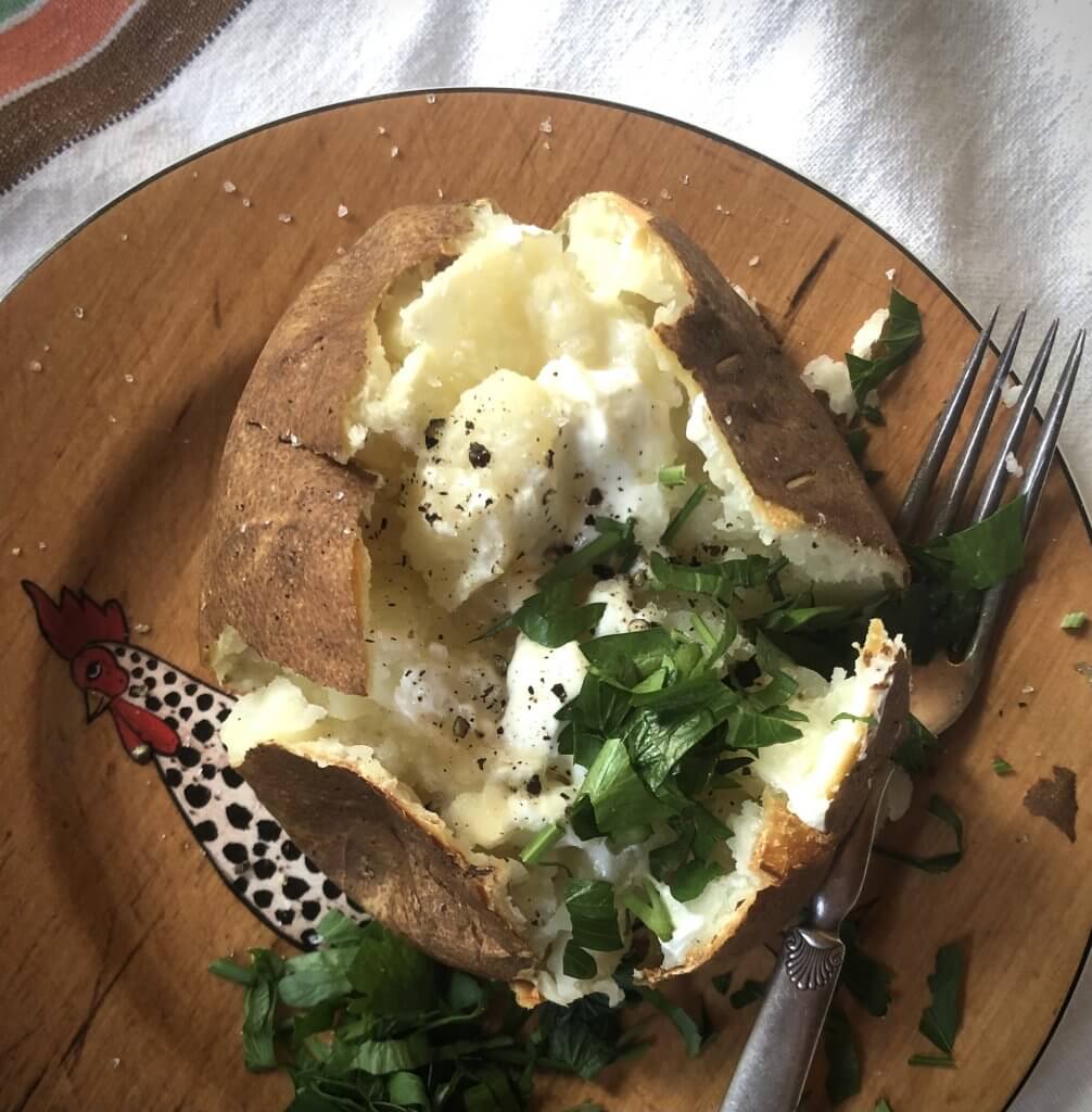 baked potato on a plate; sprinkled with salt pepper and herbs