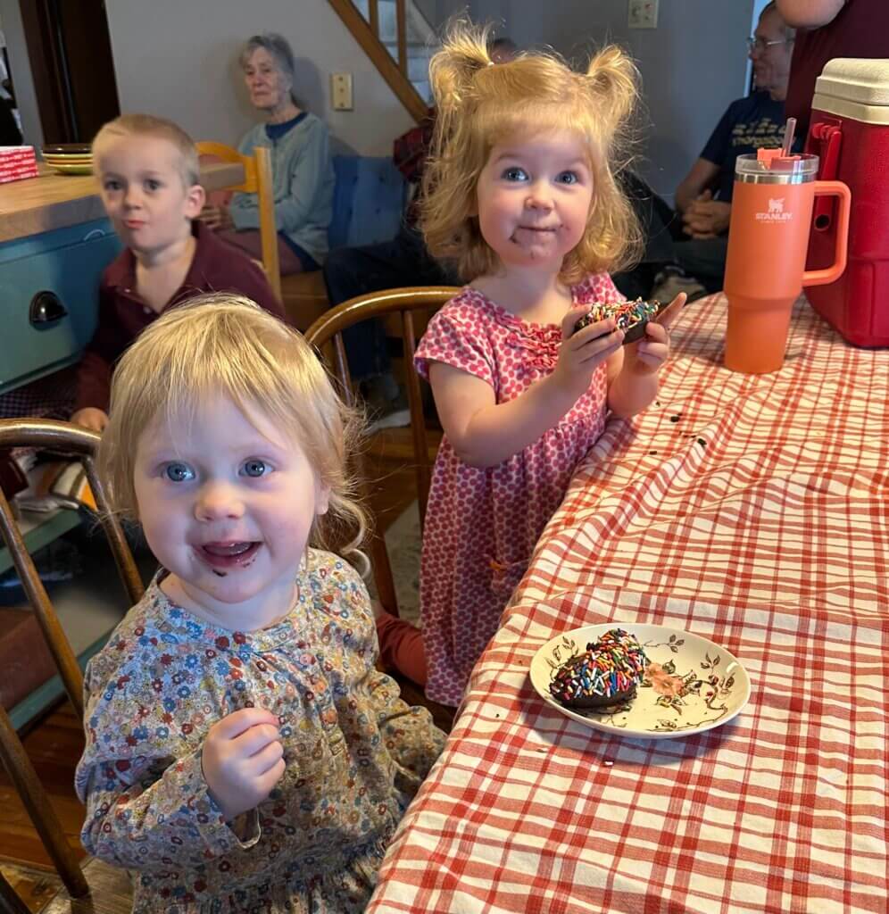 Three happy children, sitting at a table, eating donuts.