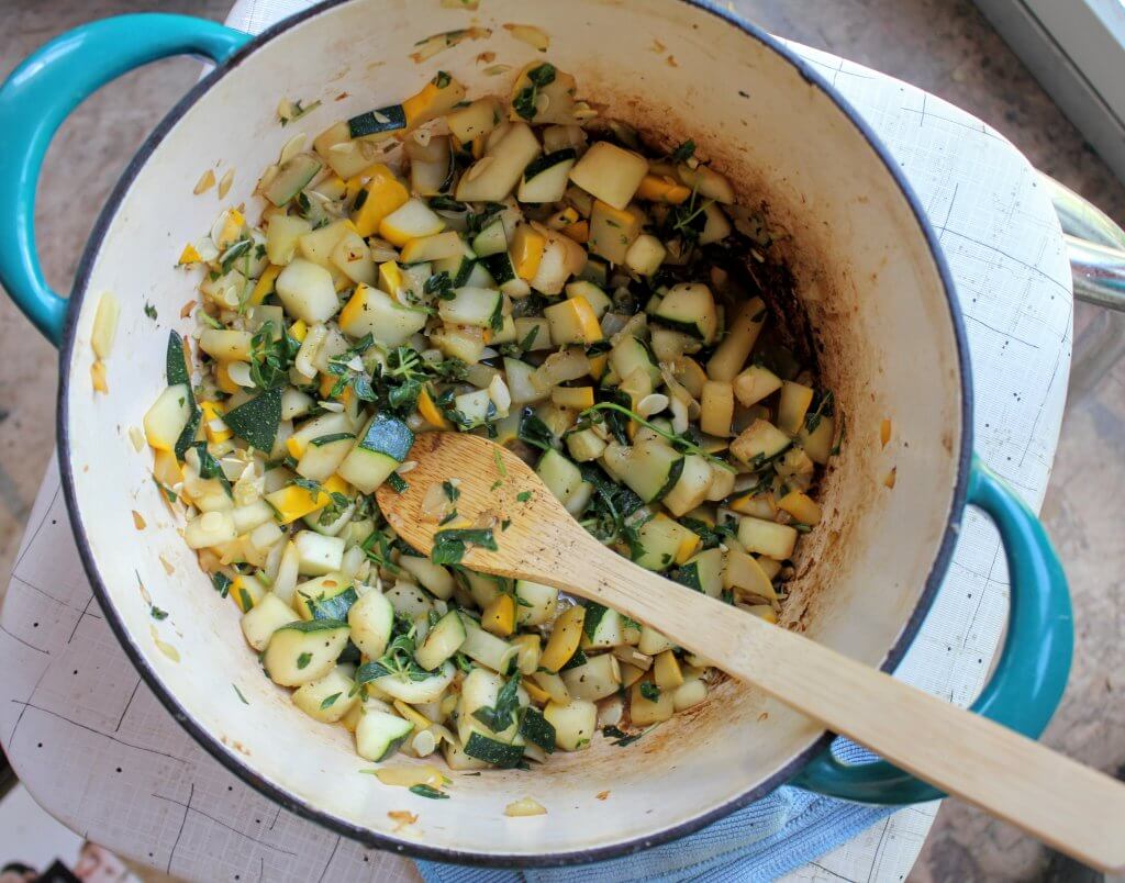 Dutch oven with sauteed and chopped summer squash and herbs.