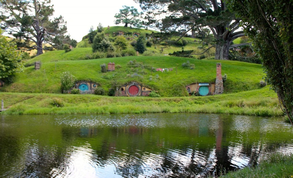 several Hobbit holes with round front doors, in front of a lake